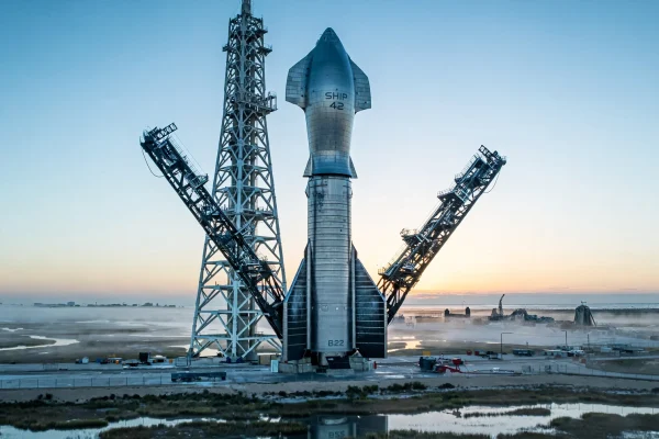 Starship Ship 42 apilado sobre el Super Heavy Booster 22 junto a la torre con los brazos de Mechazilla al amanecer