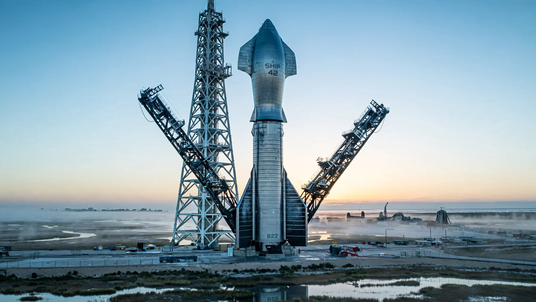 Starship Ship 42 apilado sobre el Super Heavy Booster 22 junto a la torre con los brazos de Mechazilla al amanecer