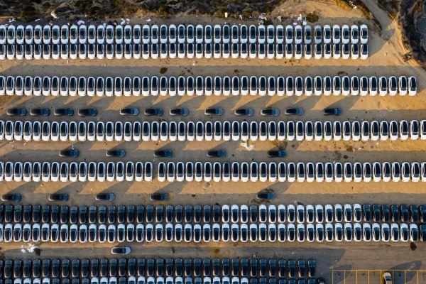 Vista cenital de una explanada portuaria al atardecer llena de filas de Tesla Model Y nuevos y un robotaxi aparte